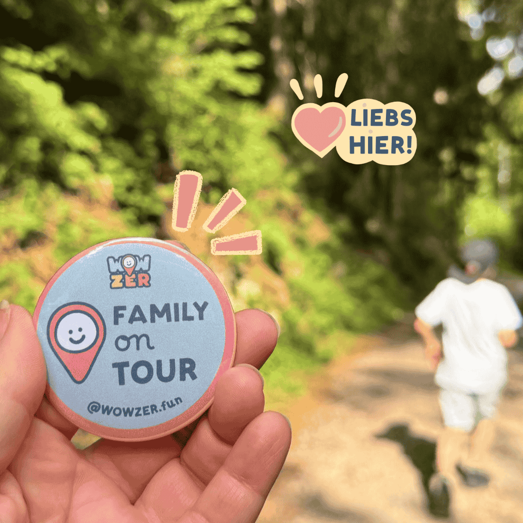 Hand hält einen WOWZER-Button „Family on Tour“ auf einem Waldweg
