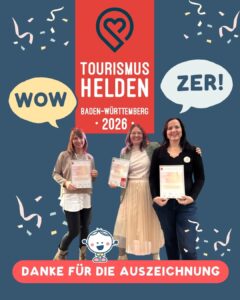 Du siehst die drei WOWZER Tourismushelden 2026 in Baden-Württemberg, die stolz ihre Urkunden zeigen und sich freuen